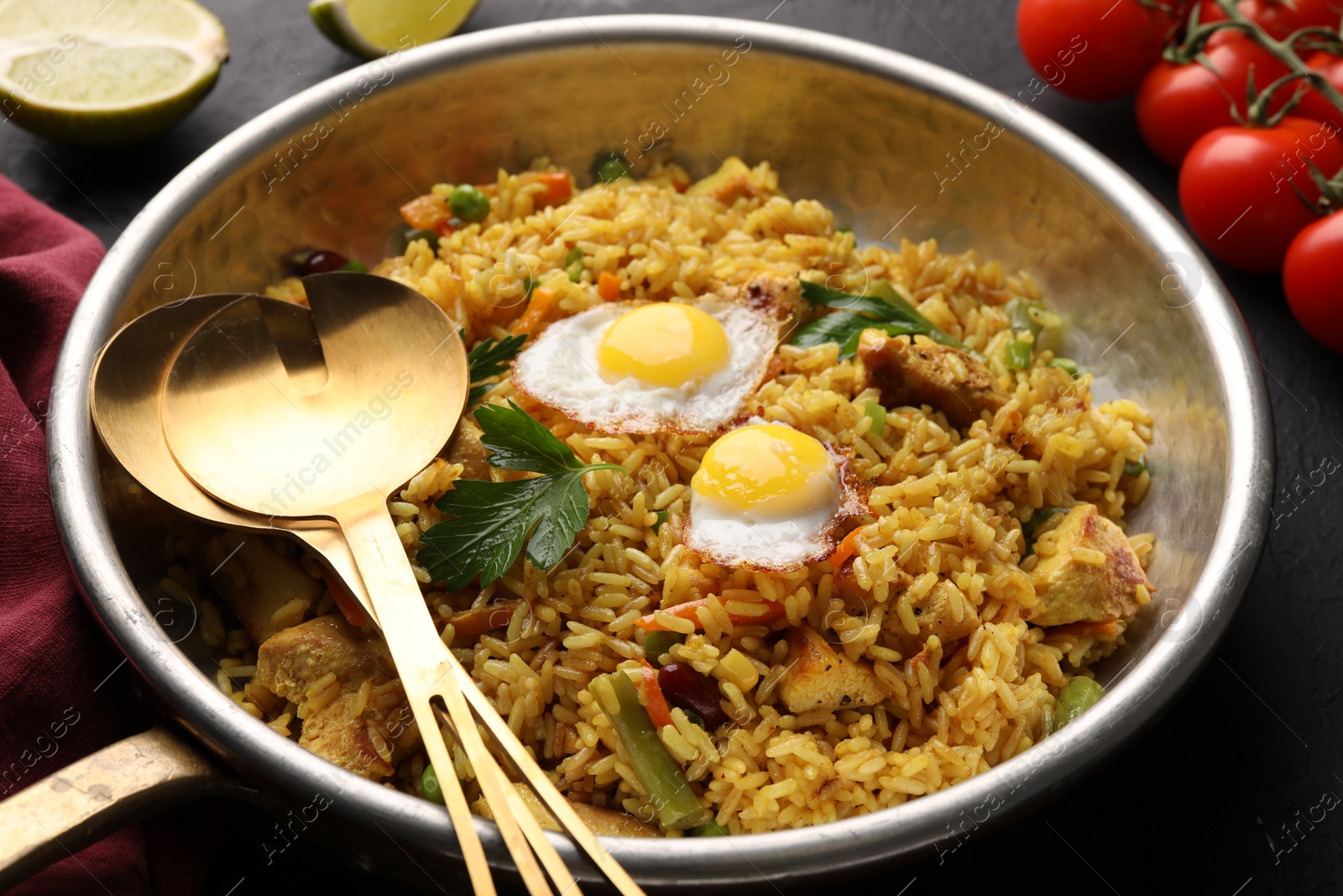 Photo of Tasty rice with meat, eggs and vegetables in frying pan near products on black table, closeup