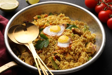 Photo of Tasty rice with meat, eggs and vegetables in frying pan near products on black table, closeup