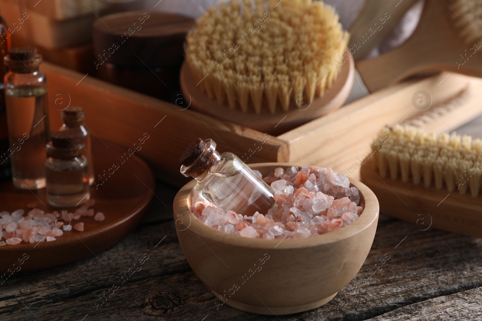 Photo of Spa composition. Bottles of cosmetic products, sea salt and brushes on wooden table, closeup