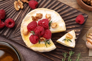 Photo of Brie cheese served with raspberries, walnuts and honey on wooden table, flat lay