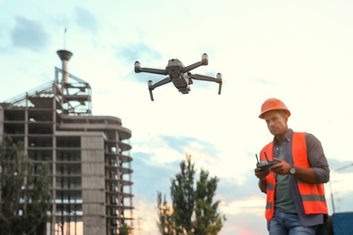 Builder operating drone with remote control at construction site, focus on quadcopter. Aerial survey