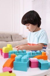 Photo of Cute little boy playing with colorful building blocks at table in living room