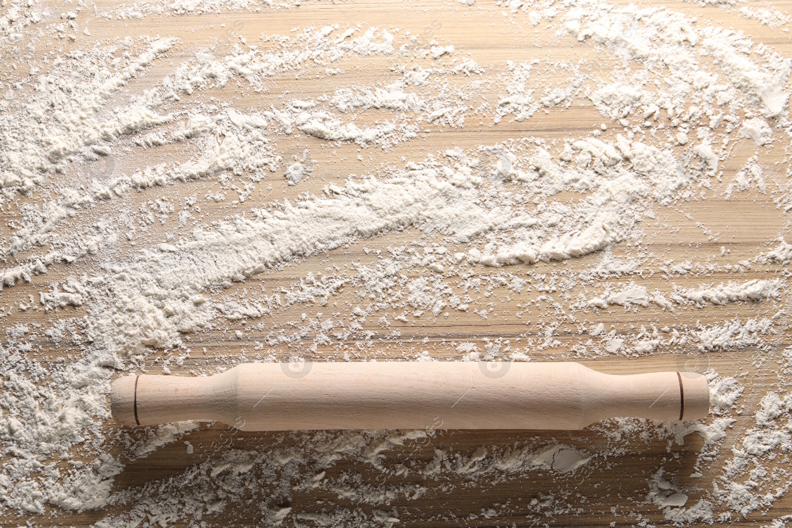 Photo of Scattered flour and rolling pin on wooden table, top view