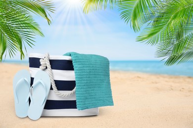 Image of Stylish bag with towel and flip flops on tropical sandy beach, space for text 