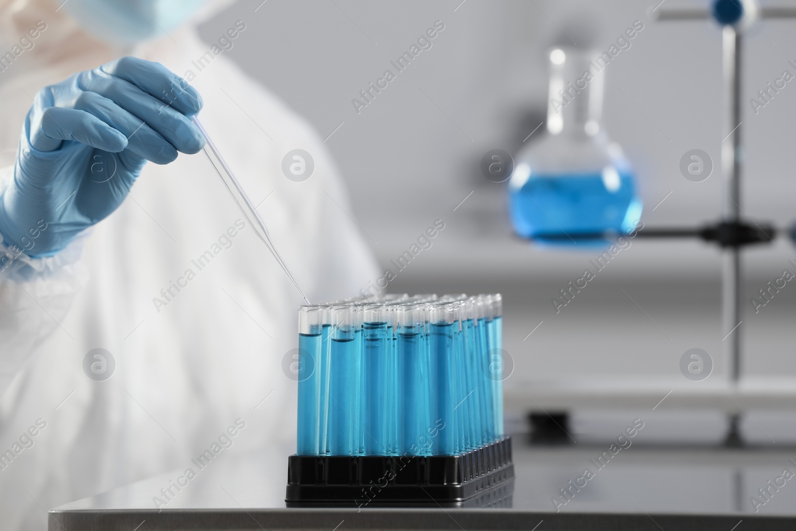 Photo of Scientist taking sample of light blue liquid in laboratory, closeup