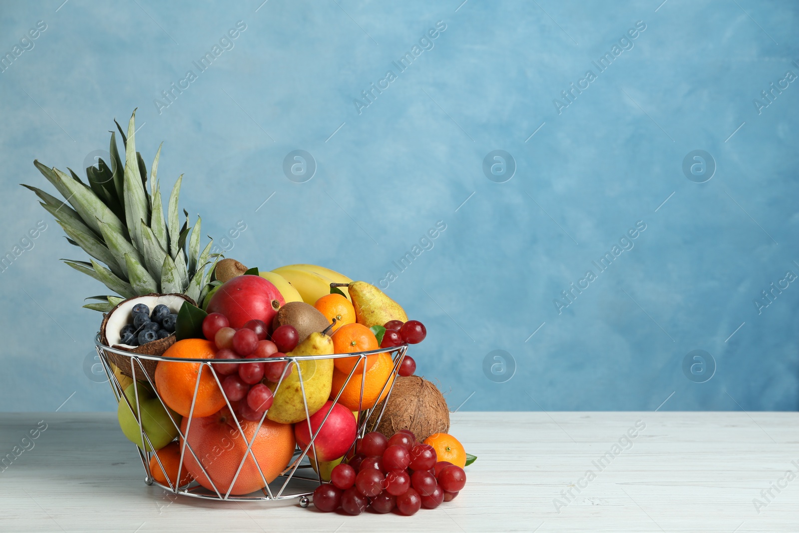 Photo of Assortment of fresh exotic fruits on white wooden table against light blue background. Space for text