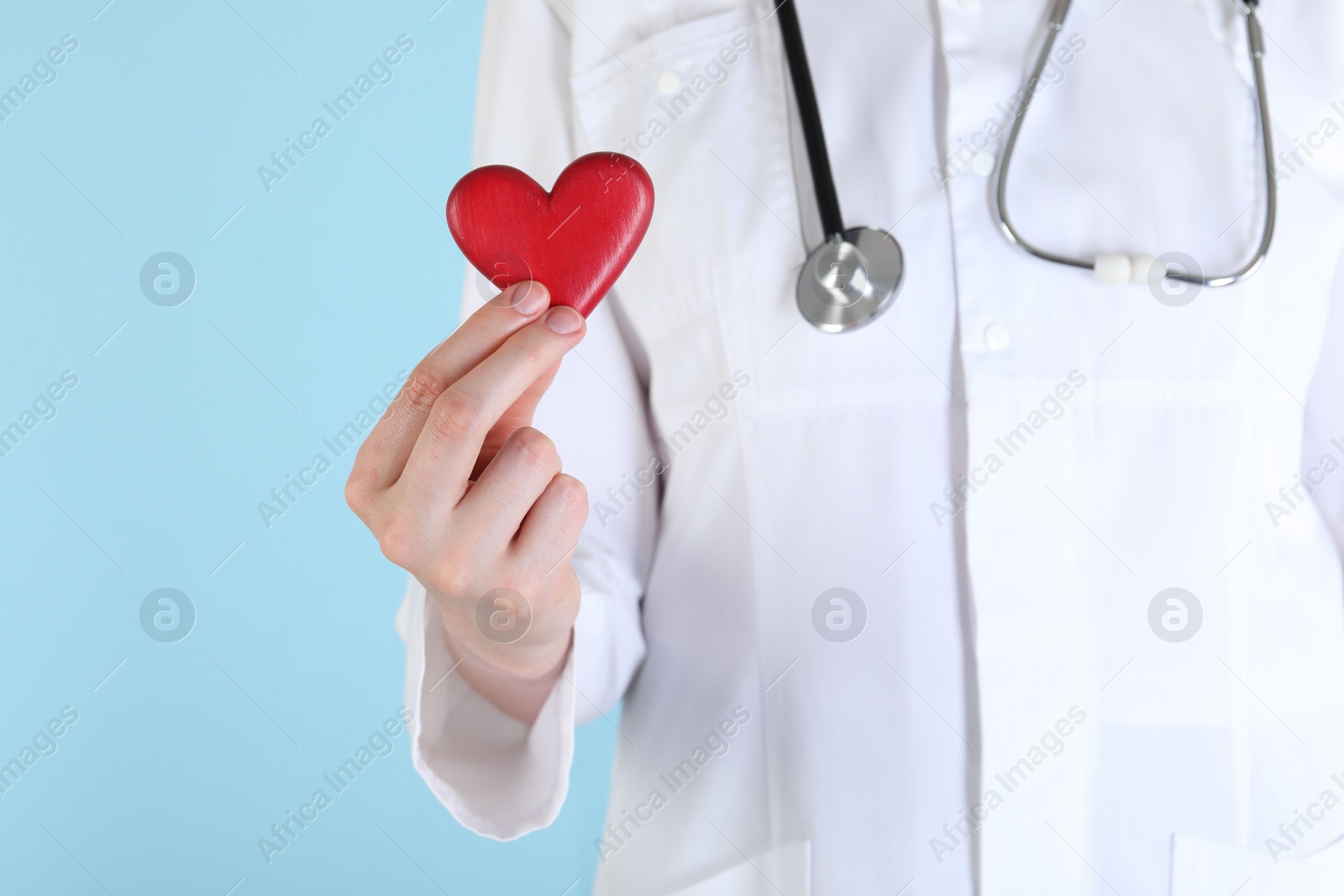 Photo of Doctor with red heart on light blue background, closeup. Space for text