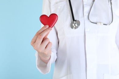 Photo of Doctor with red heart on light blue background, closeup. Space for text