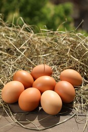 Photo of Fresh chicken eggs and dried hay on wooden table outdoors