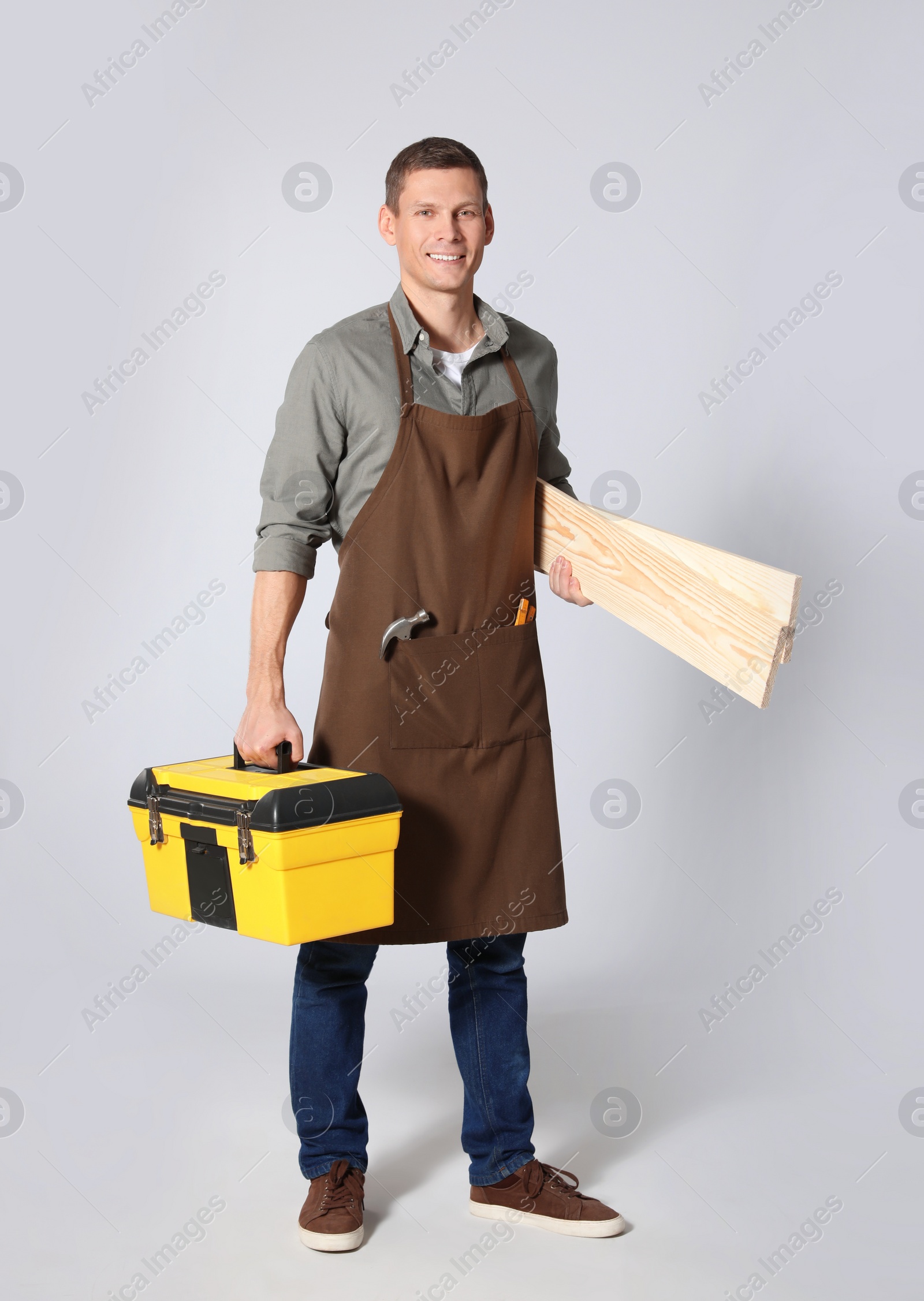 Photo of Handsome carpenter with wooden planks and tool box on light grey background