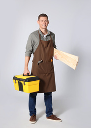 Handsome carpenter with wooden planks and tool box on light grey background