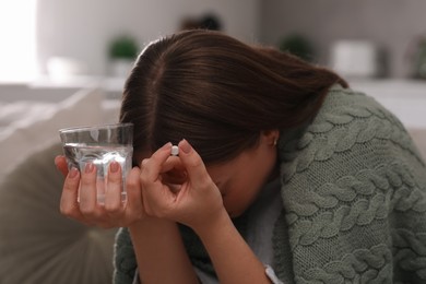 Photo of Depressed woman with antidepressant pill and glass of water indoors