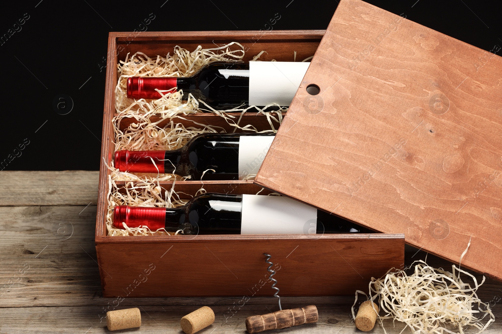 Photo of Box with wine bottles, corkscrew and corks on wooden table against black background