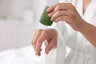 Young woman applying aloe gel from leaf onto her hand indoors, closeup. Space for text