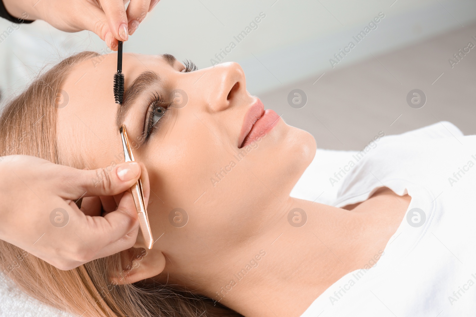 Photo of Young woman having professional eyebrow correction procedure in beauty salon