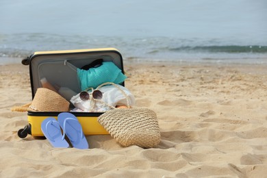 Open suitcase with beach items on sandy seashore, space for text