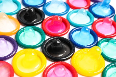 Photo of Unpacked colorful condoms on white background, closeup. Safe sex