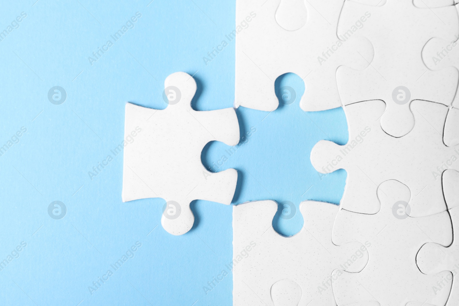 Photo of Blank white puzzle with separated piece on light blue background, flat lay