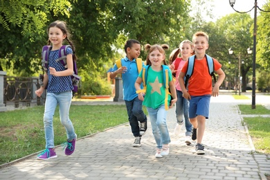 Photo of Cute little children with backpacks running outdoors. Elementary school