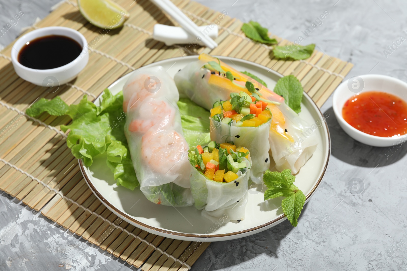 Photo of Tasty spring rolls and sauces on grey textured table, closeup