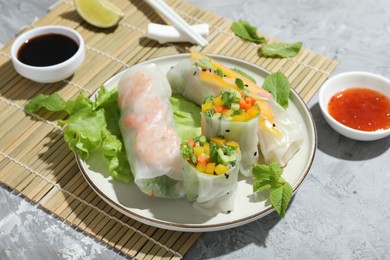 Photo of Tasty spring rolls and sauces on grey textured table, closeup