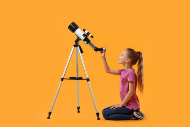 Photo of Happy little girl with telescope on orange background