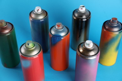 Photo of Used cans of spray paints on light blue background