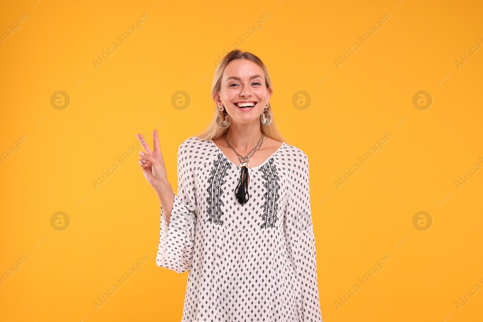 Photo of Portrait of smiling hippie woman showing peace sign on yellow background