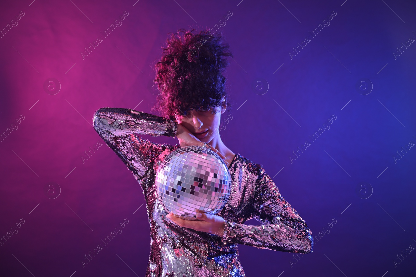 Photo of Beautiful young woman with disco ball posing on color background in neon lights