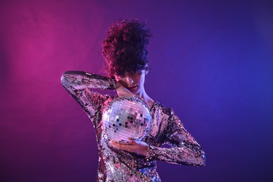 Photo of Beautiful young woman with disco ball posing on color background in neon lights