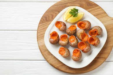 Photo of Delicious cooked snails with lemon and parsley on white wooden table, top view. Space for text