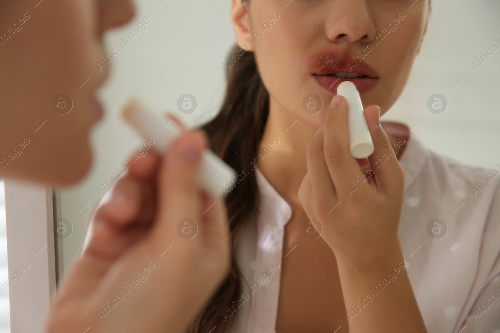 Photo of Woman with herpes applying lip balm in front of mirror, closeup