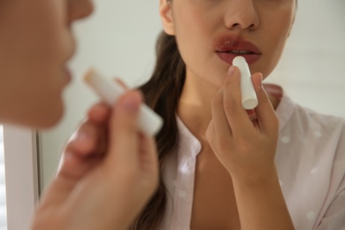 Photo of Woman with herpes applying lip balm in front of mirror, closeup