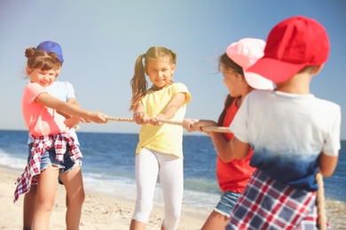 Cute children pulling rope during tug of war game on beach. Summer camp