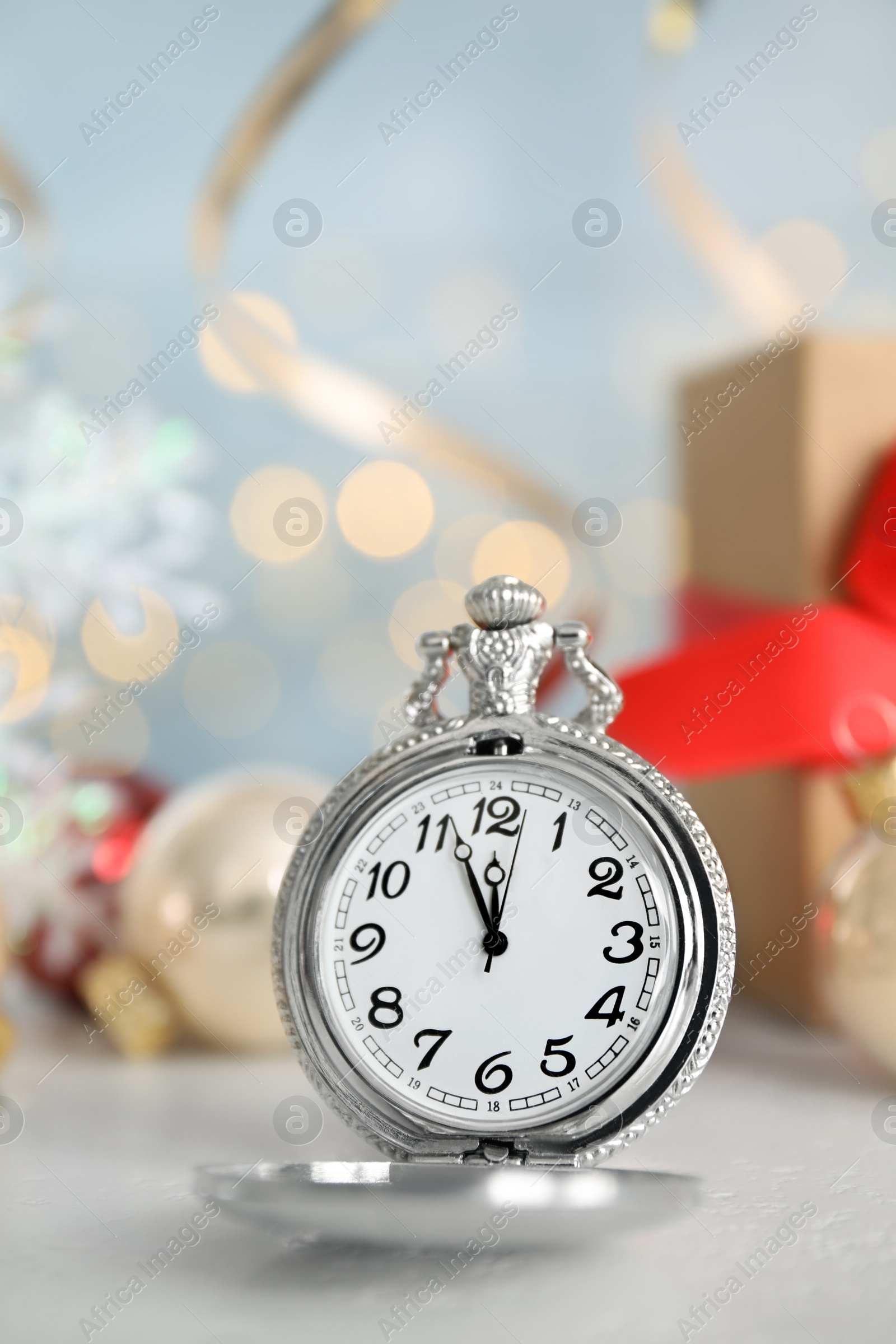 Photo of Pocket watch and festive decor on table against blurred lights, space for text. New Year countdown