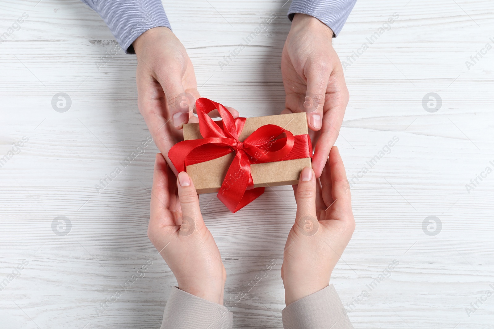 Photo of Man giving gift box to woman on white wooden table, top view