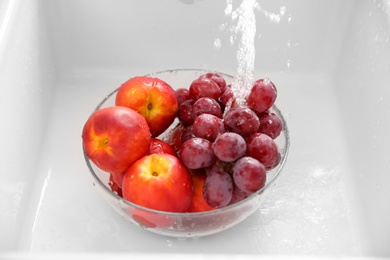 Photo of Washing fresh grapes and nectarines in bowl under tap water