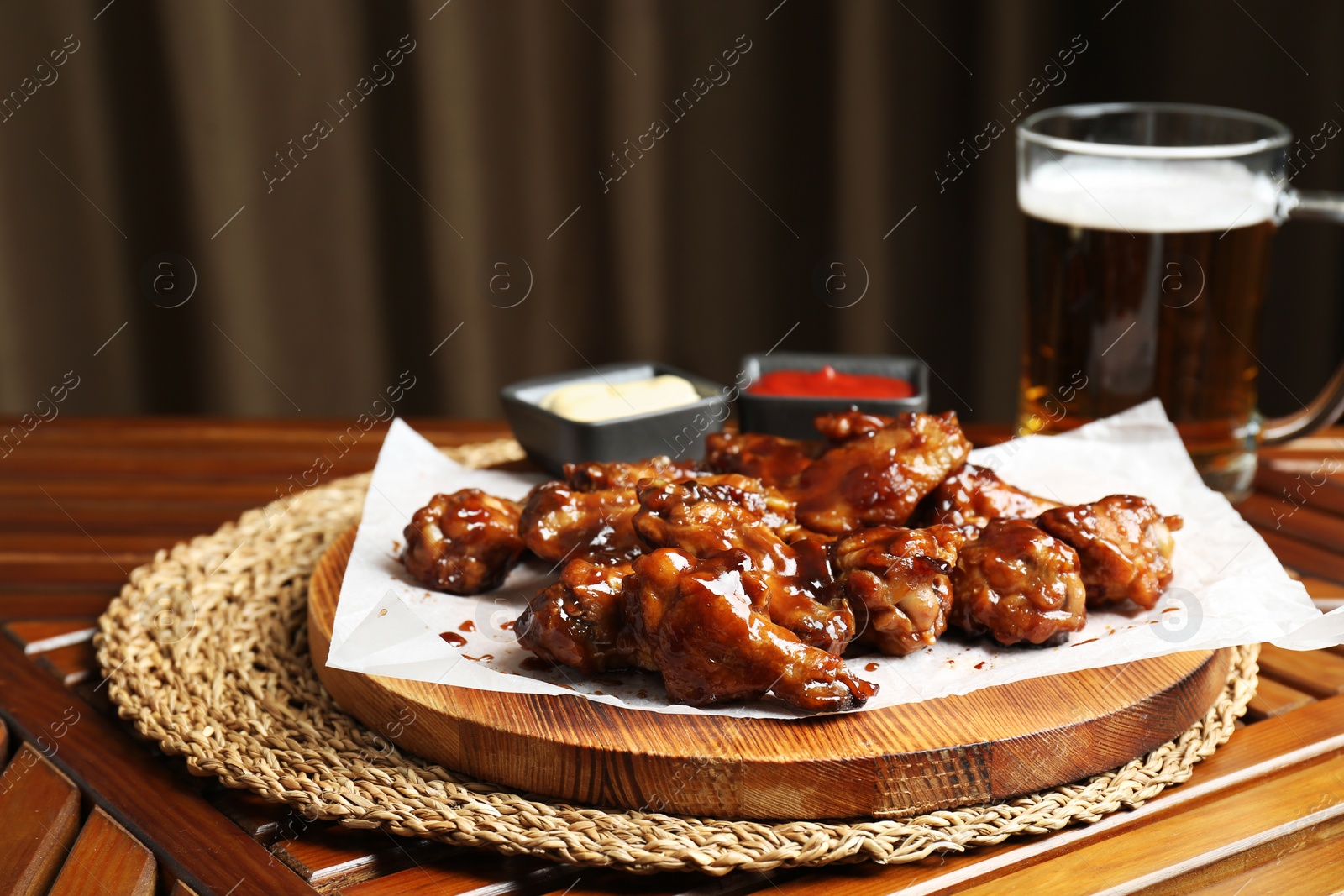 Photo of Tasty chicken wings, sauces and mug of beer on wooden table, space for text. Delicious snack