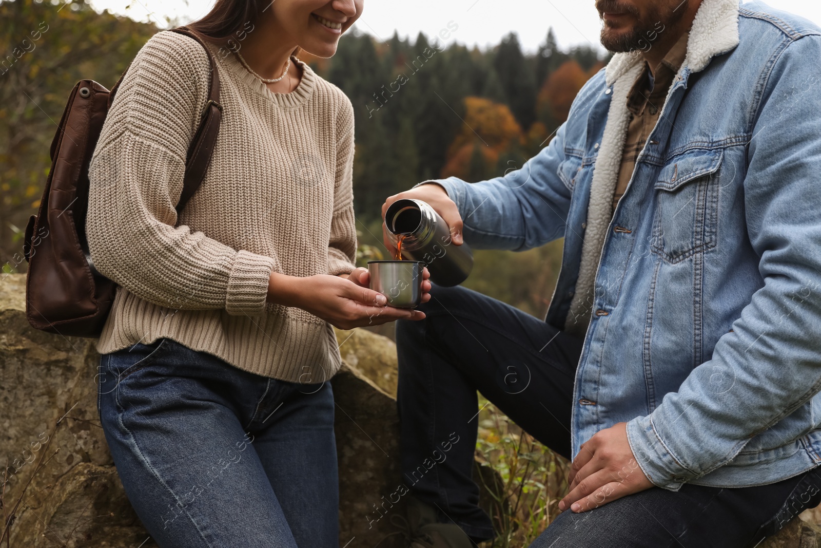 Photo of Boyfriend pouring hot drink from metallic thermos into cup lid for his girlfriend outdoors, closeup