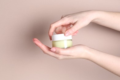 Photo of Woman with jar of cream on beige background, closeup