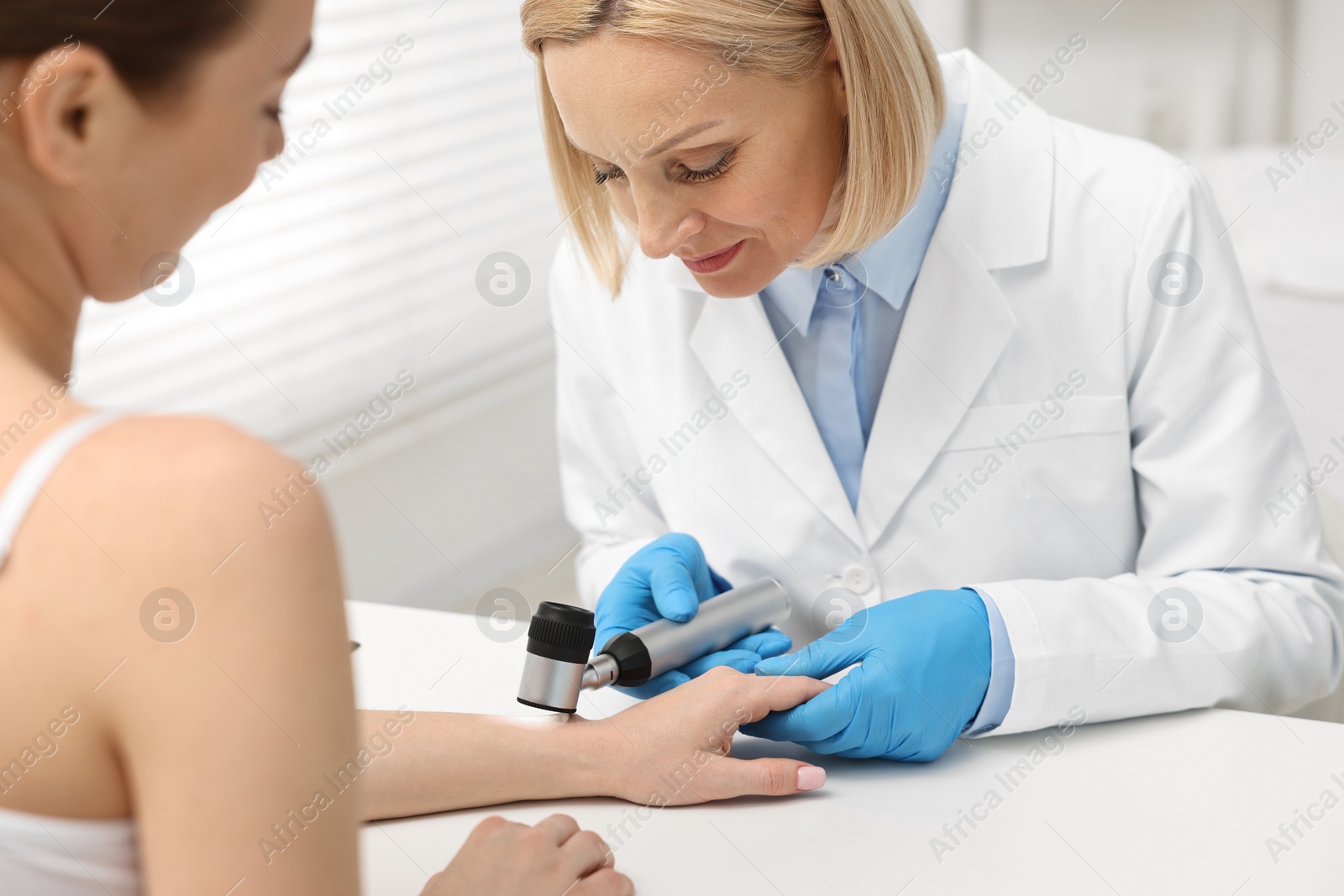 Photo of Dermatologist with dermatoscope examining patient at white table in clinic