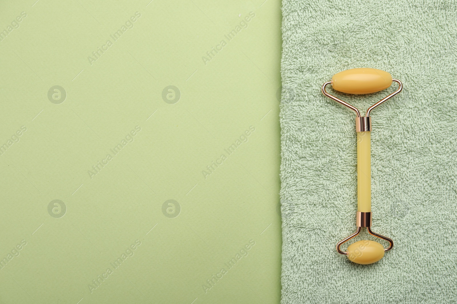 Photo of Natural face roller and towel on green background, top view. Space for text