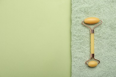 Natural face roller and towel on green background, top view. Space for text