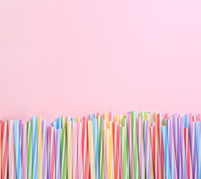 Heap of colorful plastic drinking straws on pink background, flat lay. Space for text