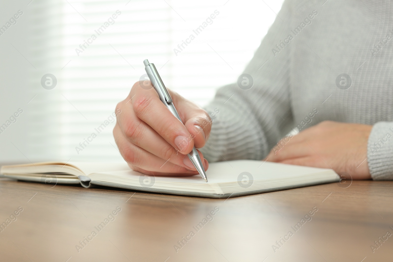 Photo of Man writing in notebook at wooden table indoors, closeup