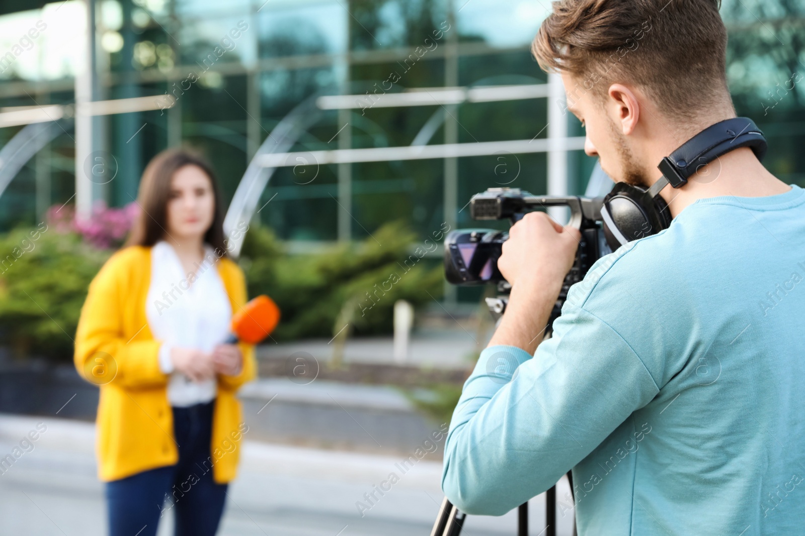 Photo of Young journalist and video operator working on city street. Space for text