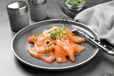 Salmon carpaccio with capers, onion and microgreens on grey table