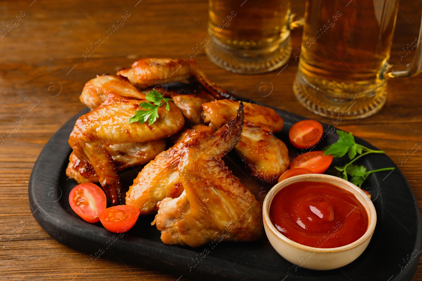 Photo of Mugs with beer, delicious baked chicken wings and sauce on wooden table