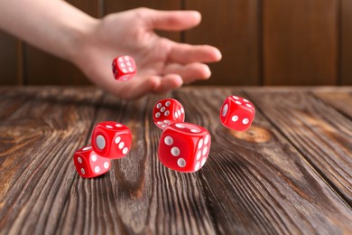 Woman throwing red dice on wooden table, closeup