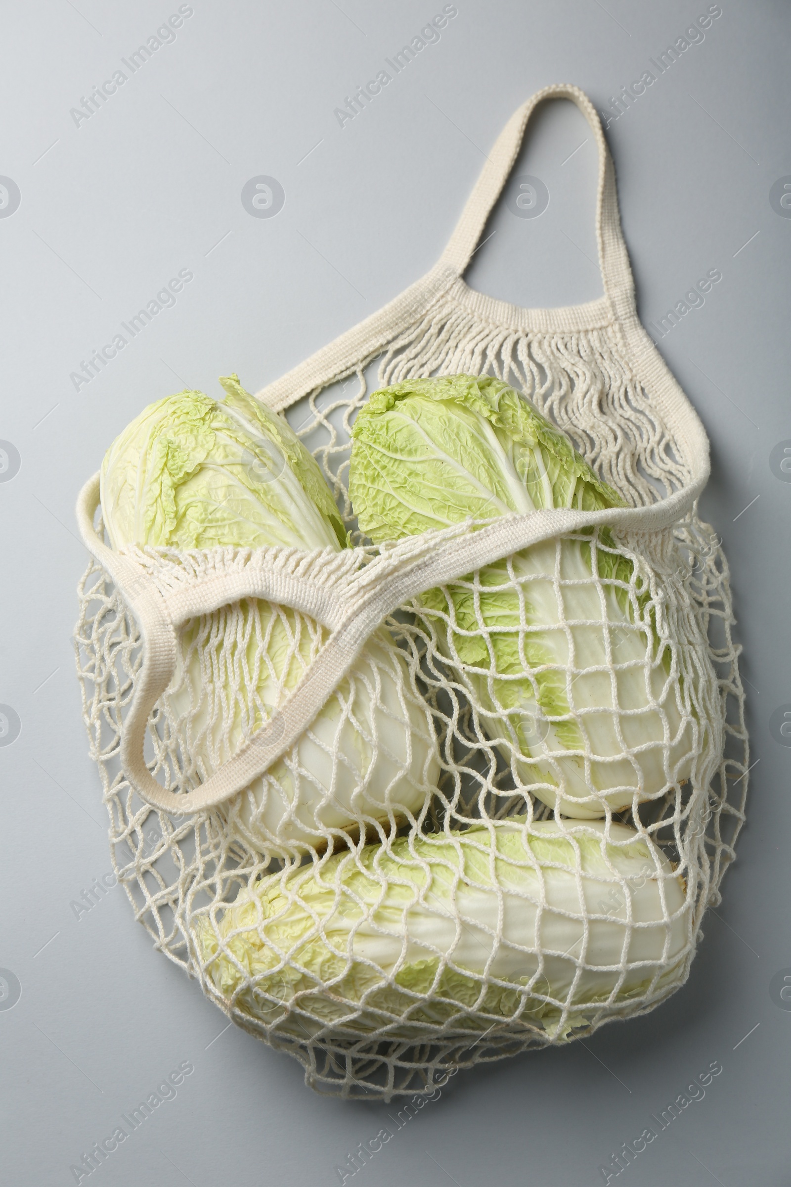 Photo of Fresh Chinese cabbages in string bag on light background, top view